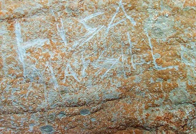detail of a portion of a cave wall with letters scratched into the surface