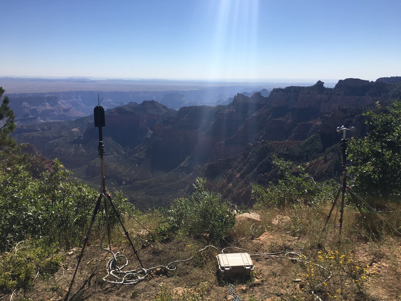 Acoustic monitoring equipment set up as tripods with wires attached are set up at the edge of the canyon.