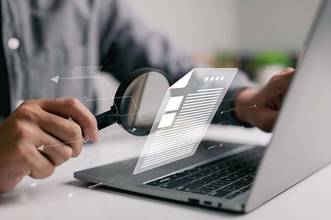 Man is inspecting a digital image that is floating above his laptop screen with a magnifier.