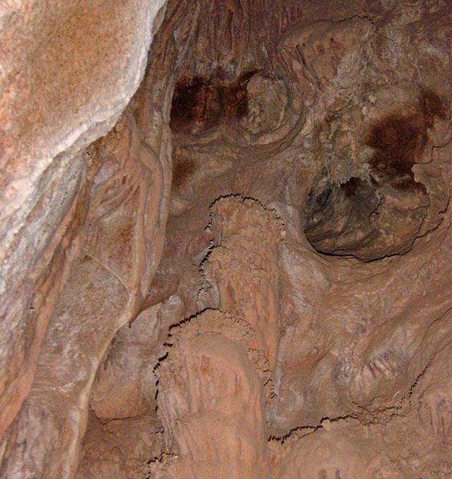 Looking up at a ceiling inside a cave. White rock is covered by a layer of beige dust. Some formations bulge out. There are also three holes in the ceiling.
