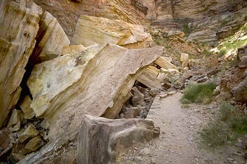 large slabs of layered sandstone rock fallen into piles alongside a backcountry train