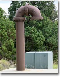 overview of well head with large brown pipe and cement pad.