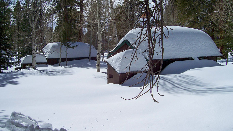 two small wood frame cabins covered with several feet of snow.