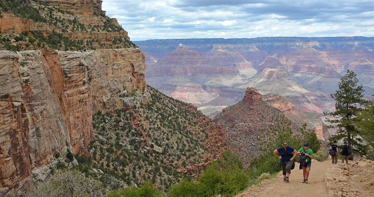 Canyon cliffs on left, to the right, 4 hikers on Bright Angel Trail. Overcast day with lots of clouds and shadows