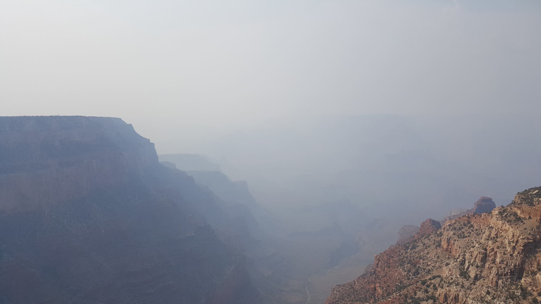 View from the rim of a canyon, past nearby cliffs into a smoke-filled interior