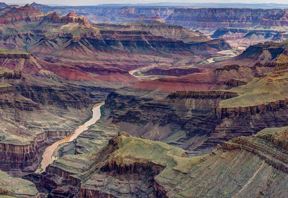 A muddy river meandering through a complex desert landscape of stratified cliffs and ridgelines.