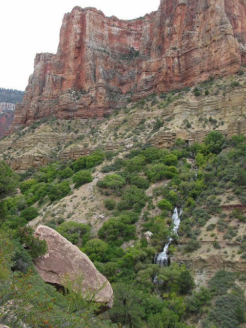 Red and tan canyon walls, with green trees and a waterfall