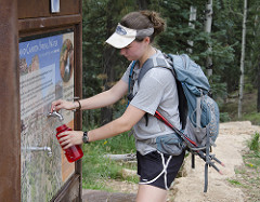 9563929331_c8dda19fcc_m hiker wearing a gray t-shirt and a white visor fills up a water bottle at the North Kaibab trailhead.