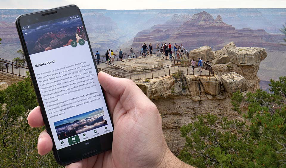 hand holding cellular phone that displays photos and text for a location. In the background, people at a scenic overlook with peak visible in the distance.