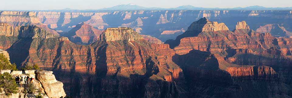 Visitors at overlook on the left looking out across Grand Canyon at three temples.