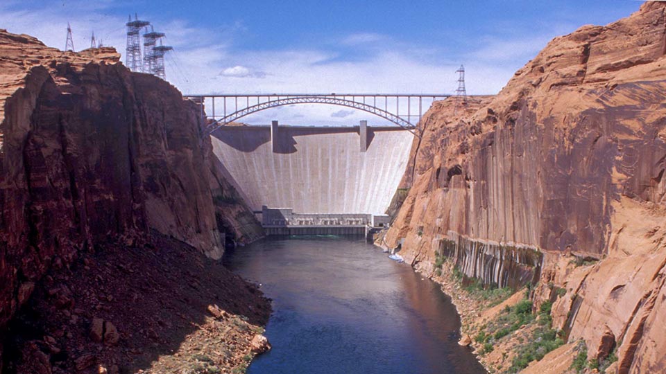 a concrete dam between sandstone cliffs with a placid blue river below.