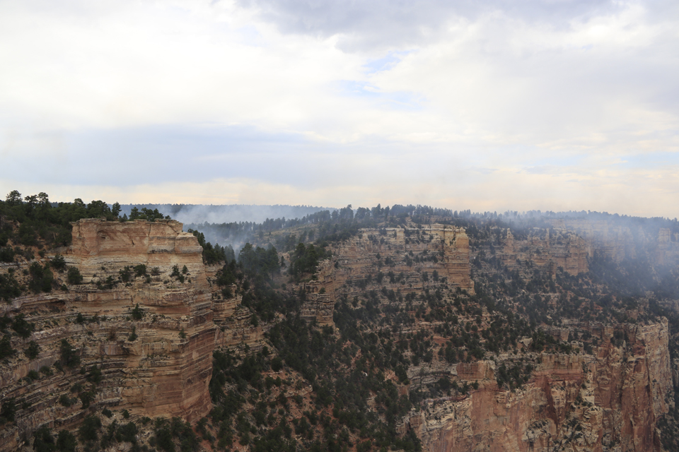 White smoke billows in from the left over the red-stained cliffs of a canyon