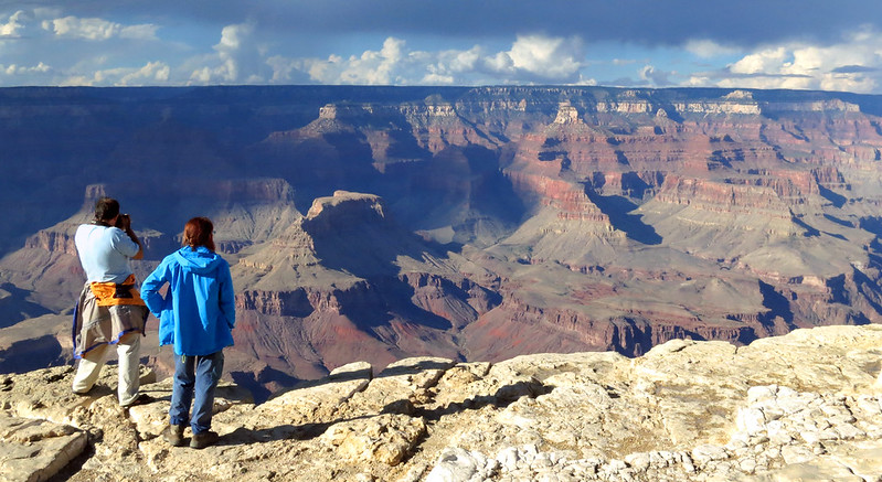Two people stand on the rim of the canyon photographing the canyon landscape