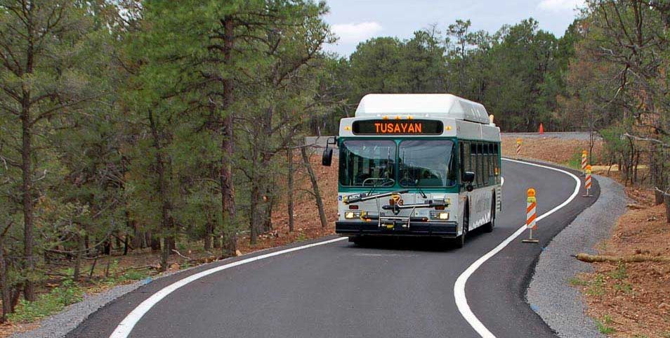 a white bus with green trim is driving on a bypass lane through a wooded area.