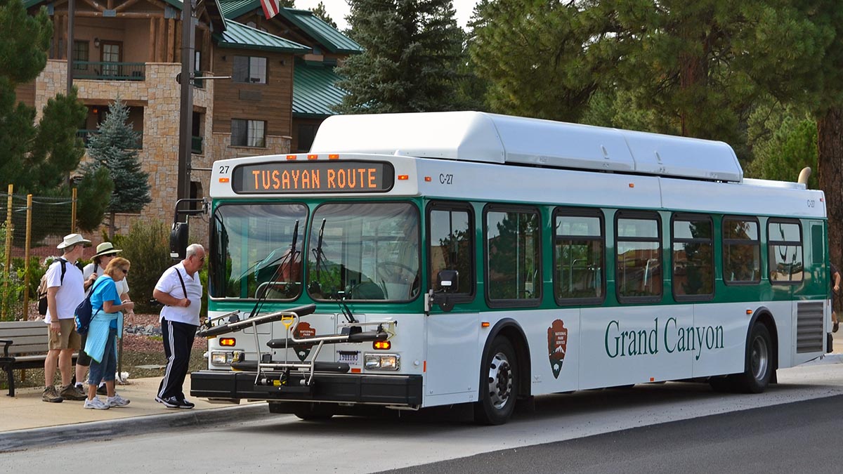 Several people boarding a green and white bus in front of a rustic lodge.