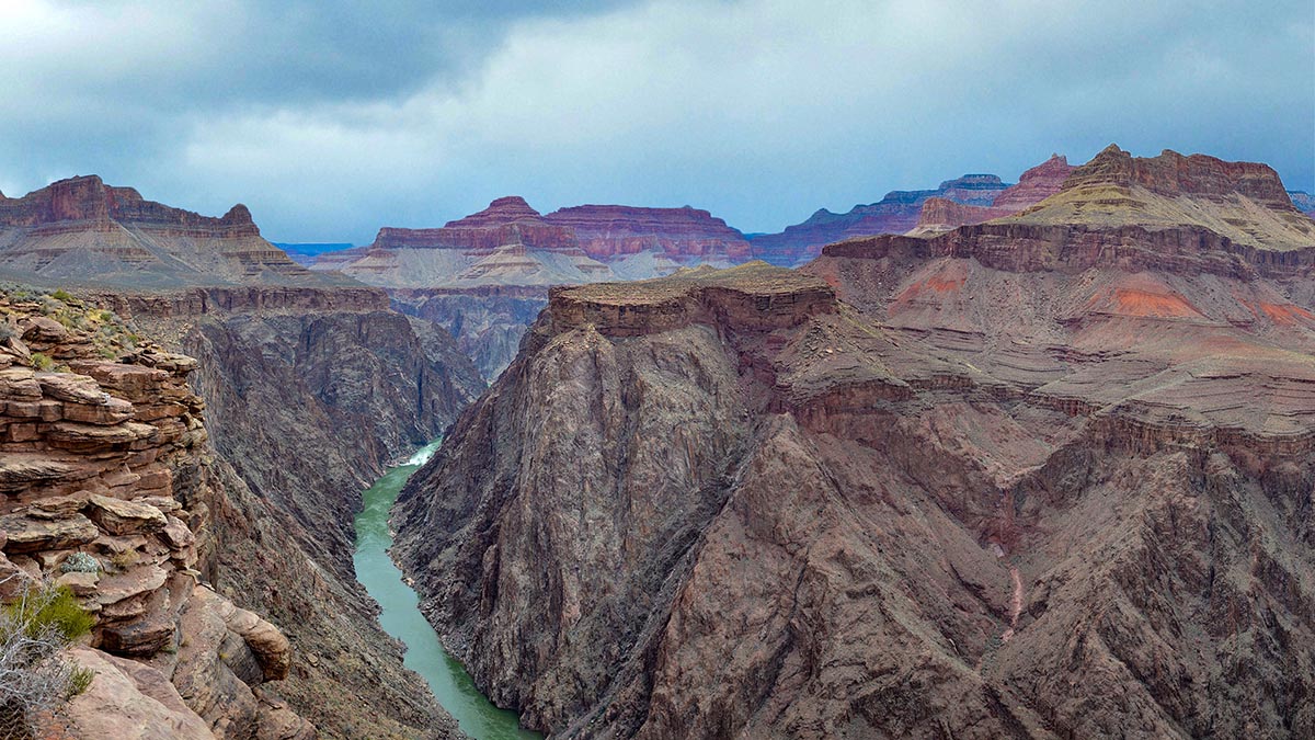 a green river flowing at the bottom of a rocky gorge with steep stone walls 1000 feet high.