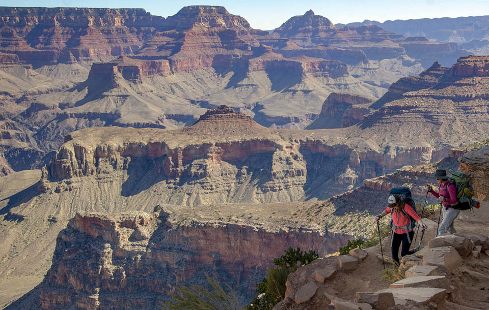 Two hikers descend down a hot, steep trail into the colorful cliffs of Grand Canyon. Two hikers descend down a hot, steep trail into the colorful cliffs of Grand Canyon.