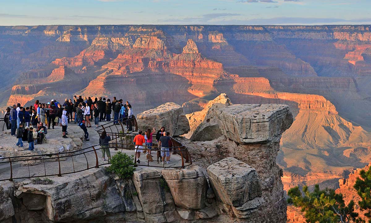 30 sightseers viewing reddish sunset light illuminating colorful peaks and cliffs in a vast canyon landscape