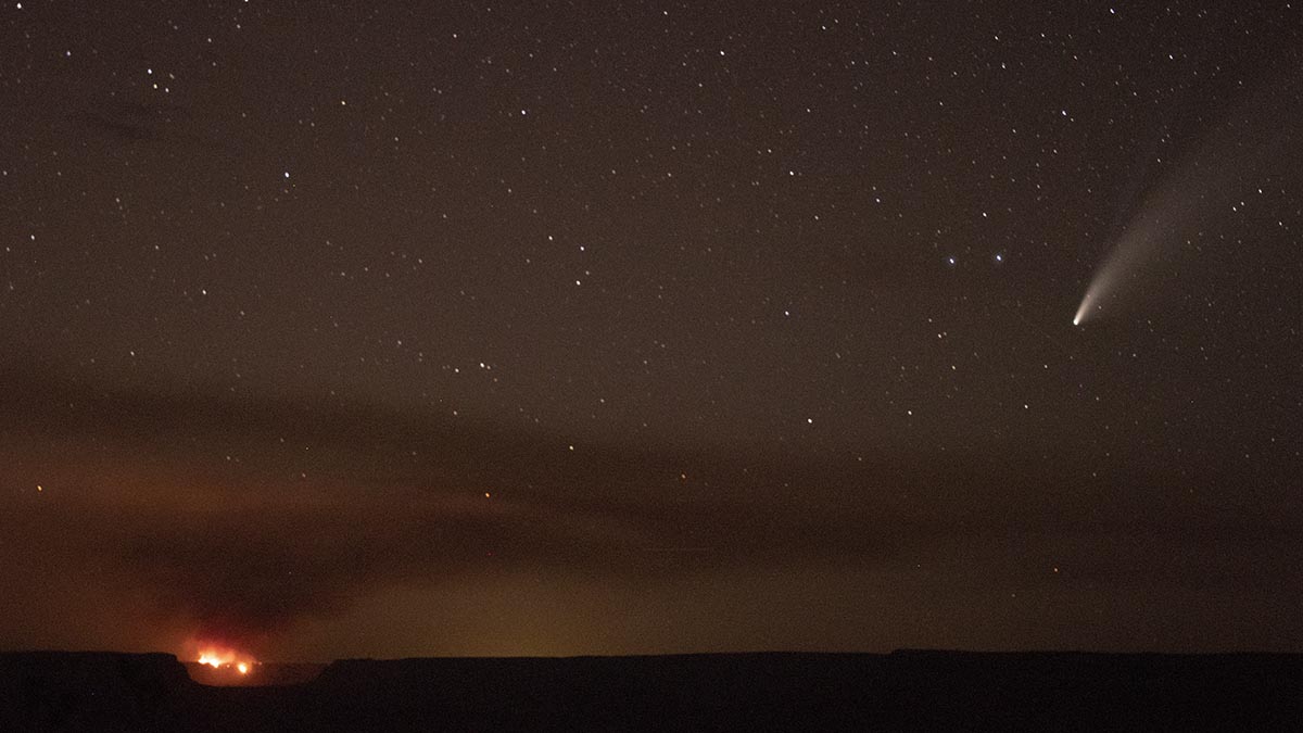 Smoke from the Thumb Fire is visible from both the North and South Rims of the park. At this time there are no closures within the park. Grand Canyon National Park is providing interagency support to the Truxton Canon Agency and the Havasupai Tribe. at night, a distant fire is seen burning on the horizon with a layer of smoke in the starry sky above. On the left, a comet with a long tail.
