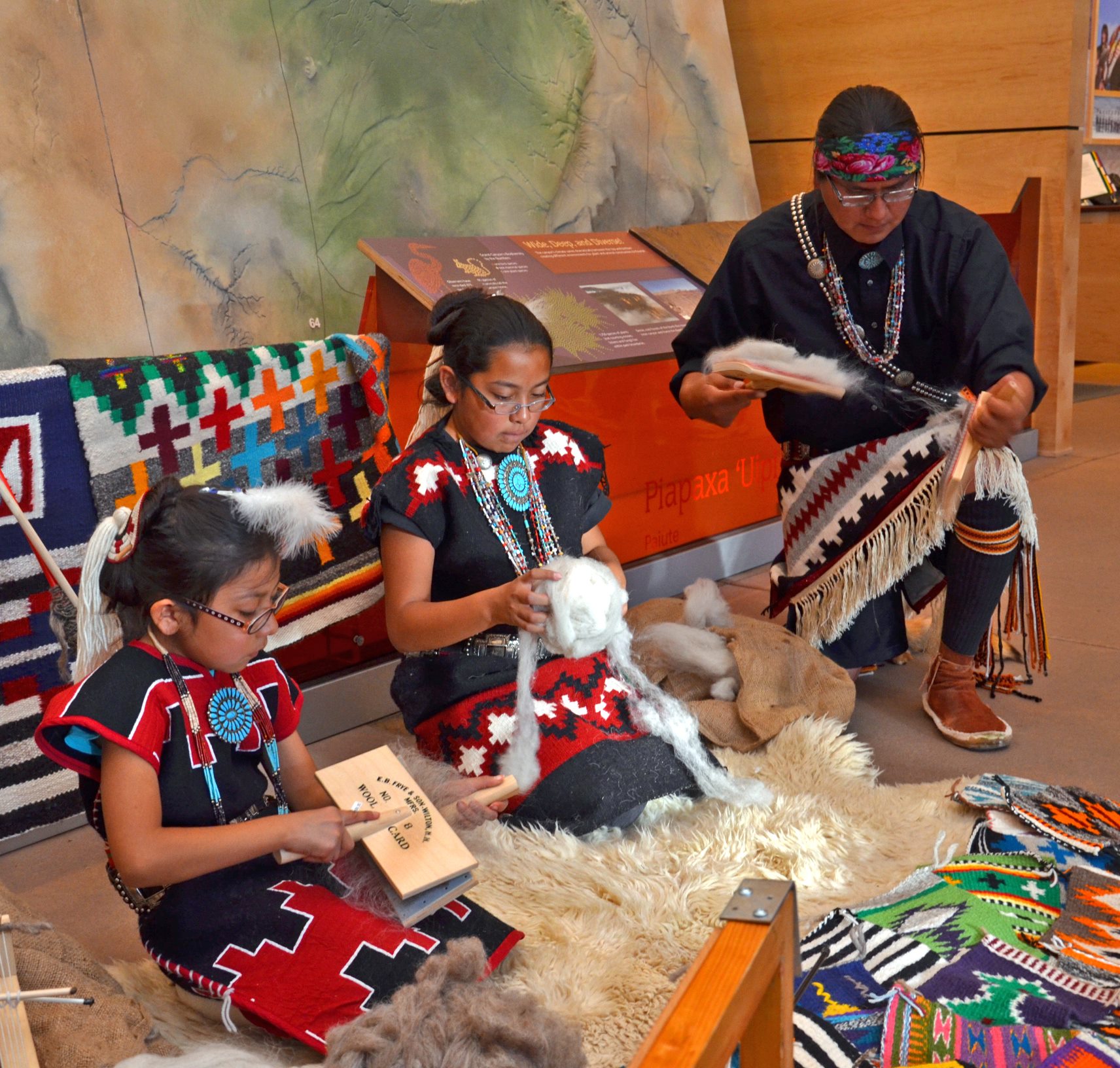 Three Dine tribal members demonstrate carding wool at the Grand Canyon Visitor Center