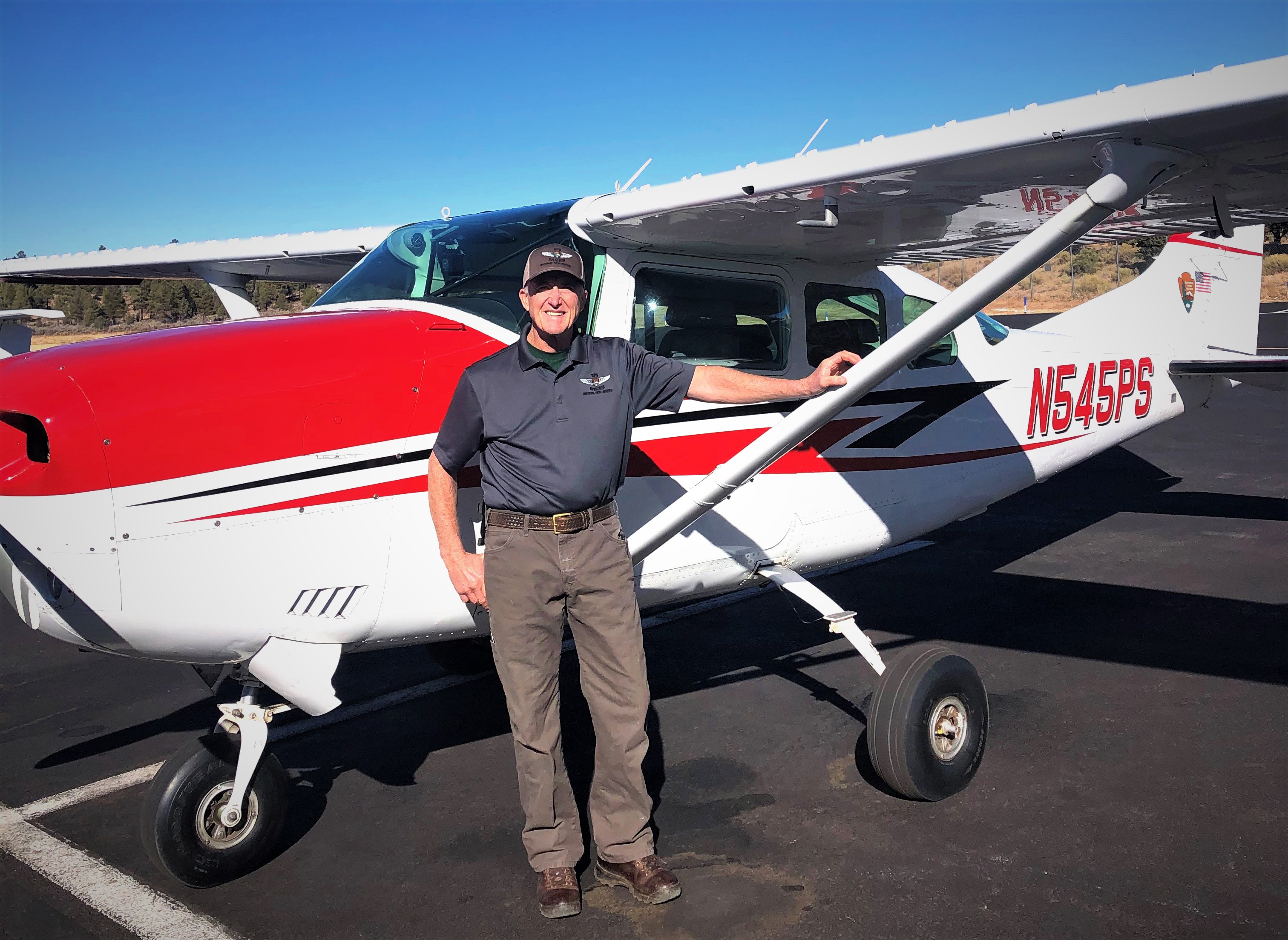 Galen Howell is seen standing next to a red and white fixed wing aircraft