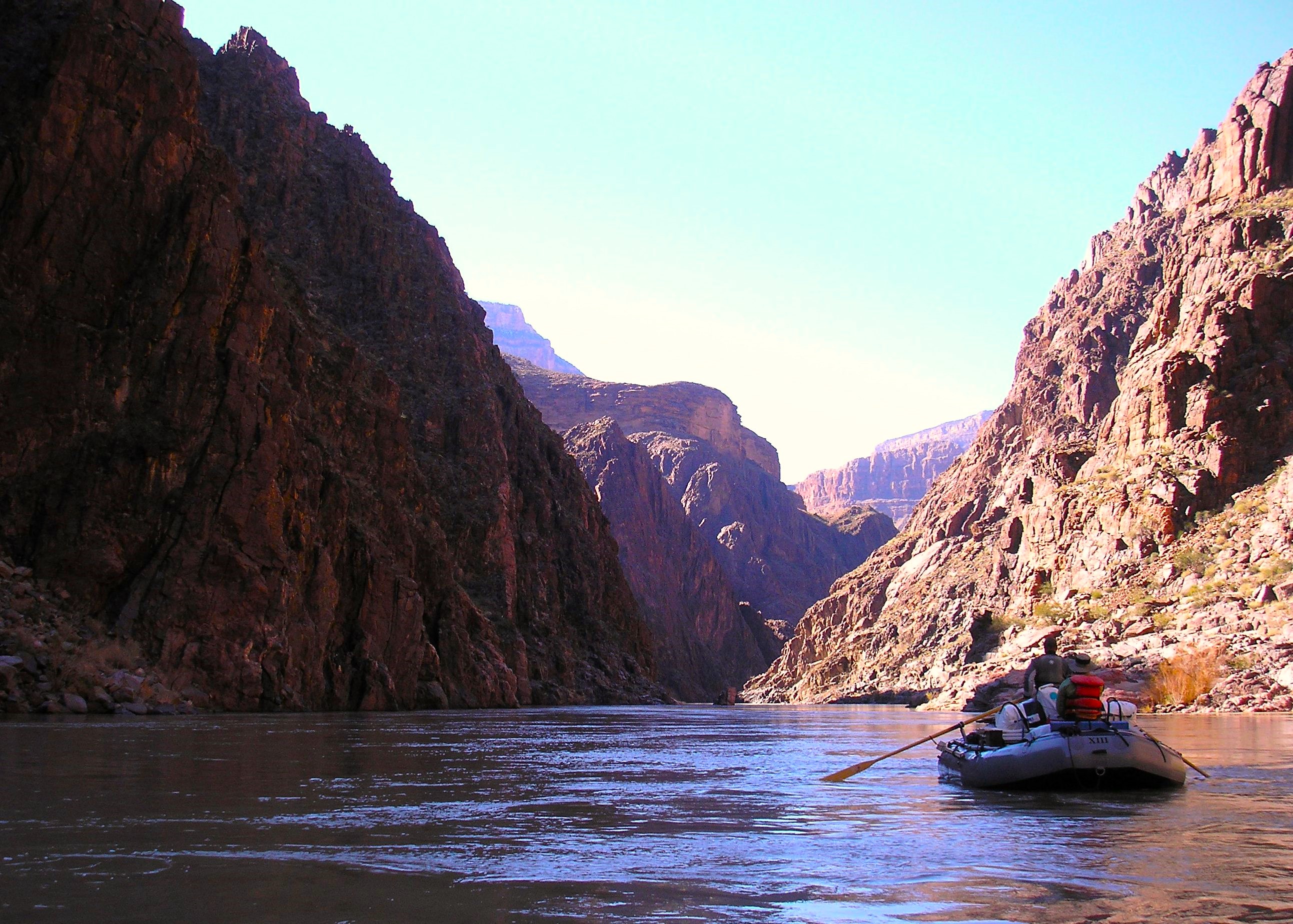 A gray boat with two passengers passes through the Granite Gorge with steep walls on each side