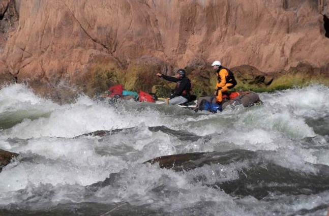Two boaters on a raft are seen navigating through rough whitewater at Granite Rapids along the Colorado River
