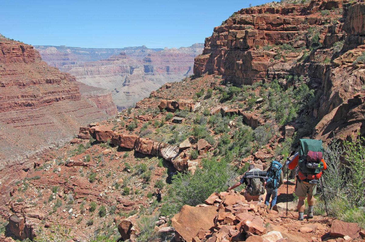 A small group of hikers with large backpacks descend down the Hermit Trail within Grand Canyon National Park