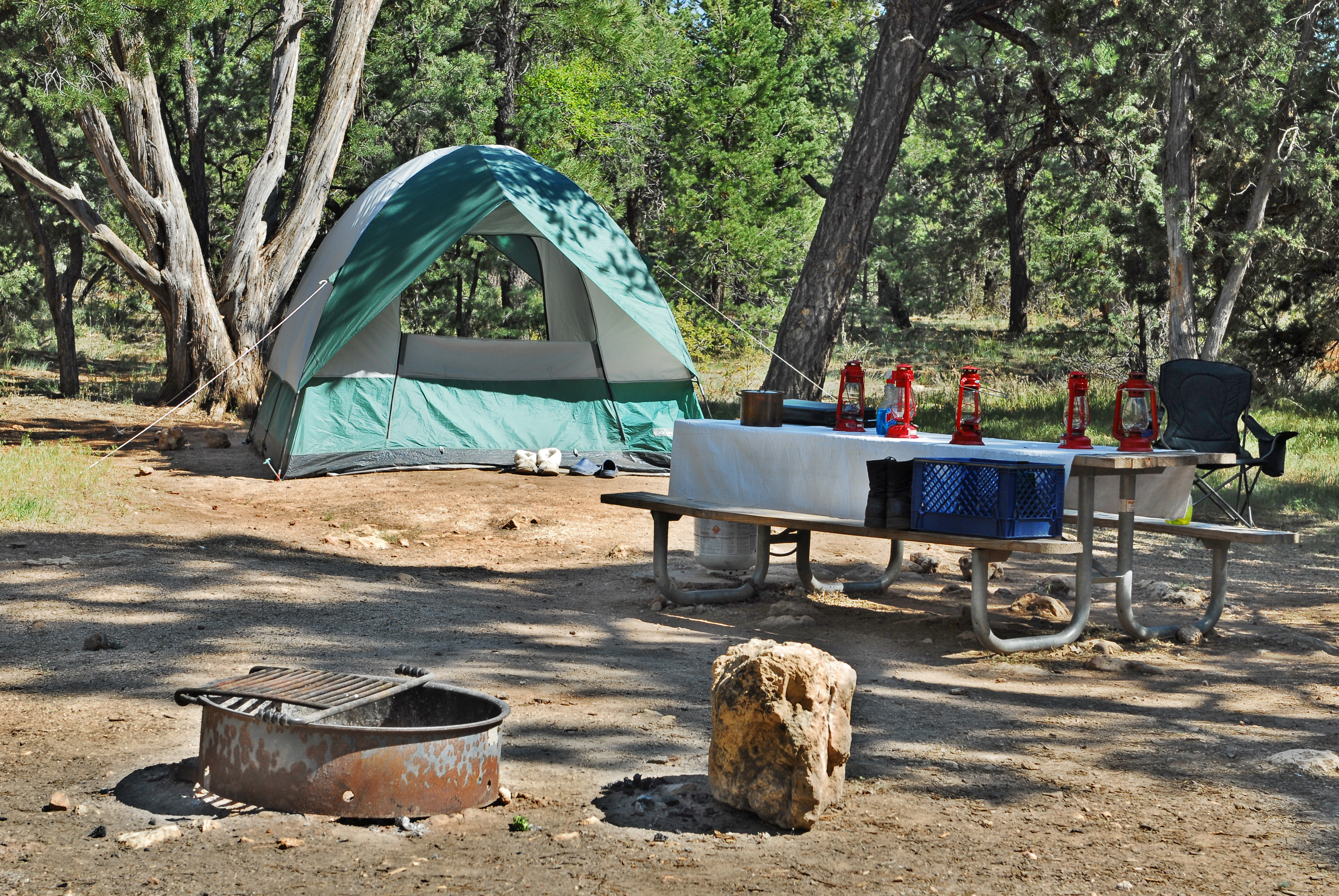 Campsite with a fire ring in the forefront, a picnic table with lanterns on it to the right, and a tent in the background.