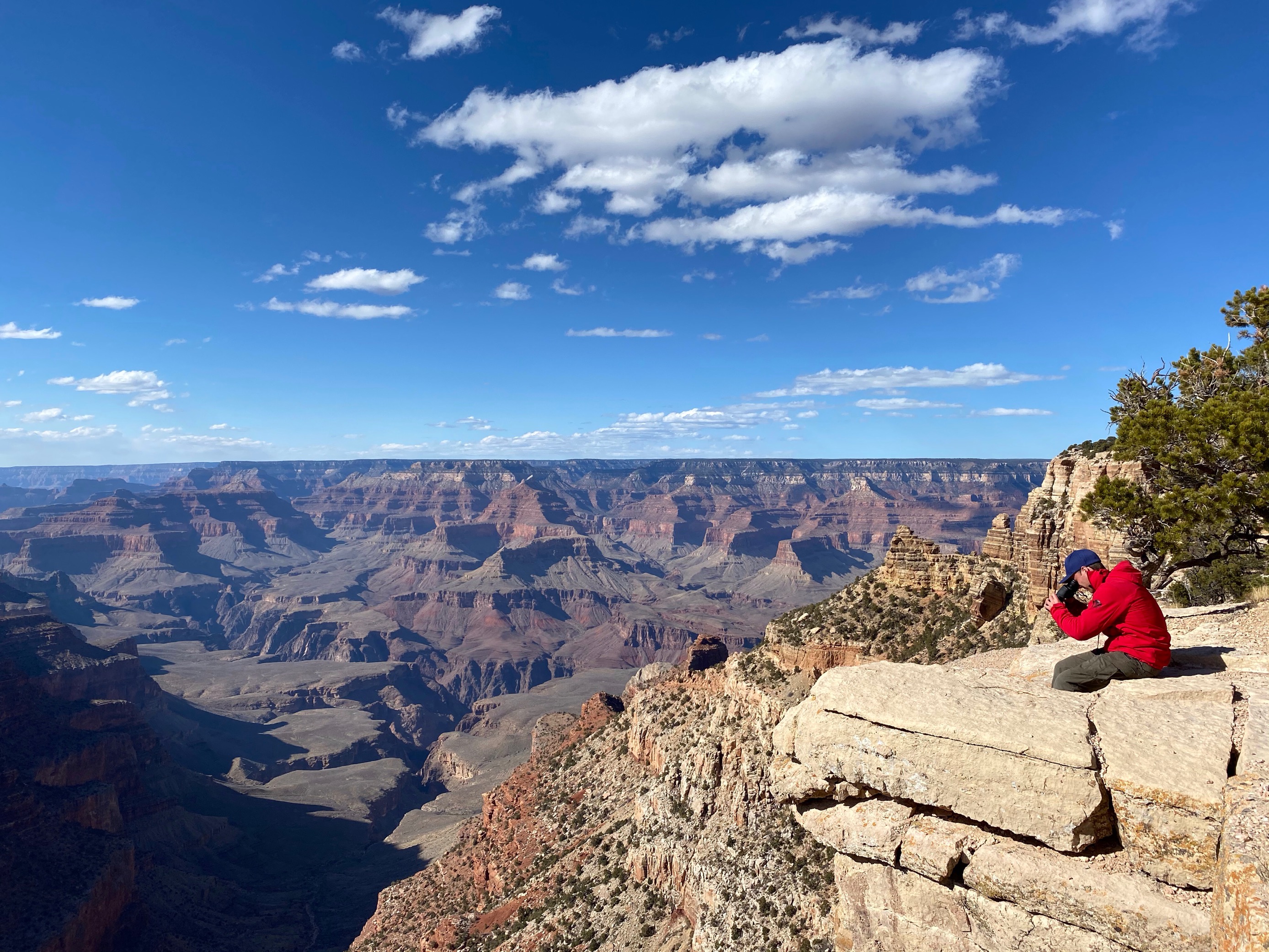 A rescuer sits at the edge of the canyon looking below the rim with binoculars