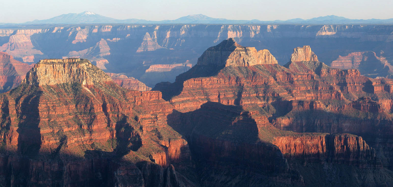 several tiny people on the left overlooking three colorful peaks within Grand Canyon