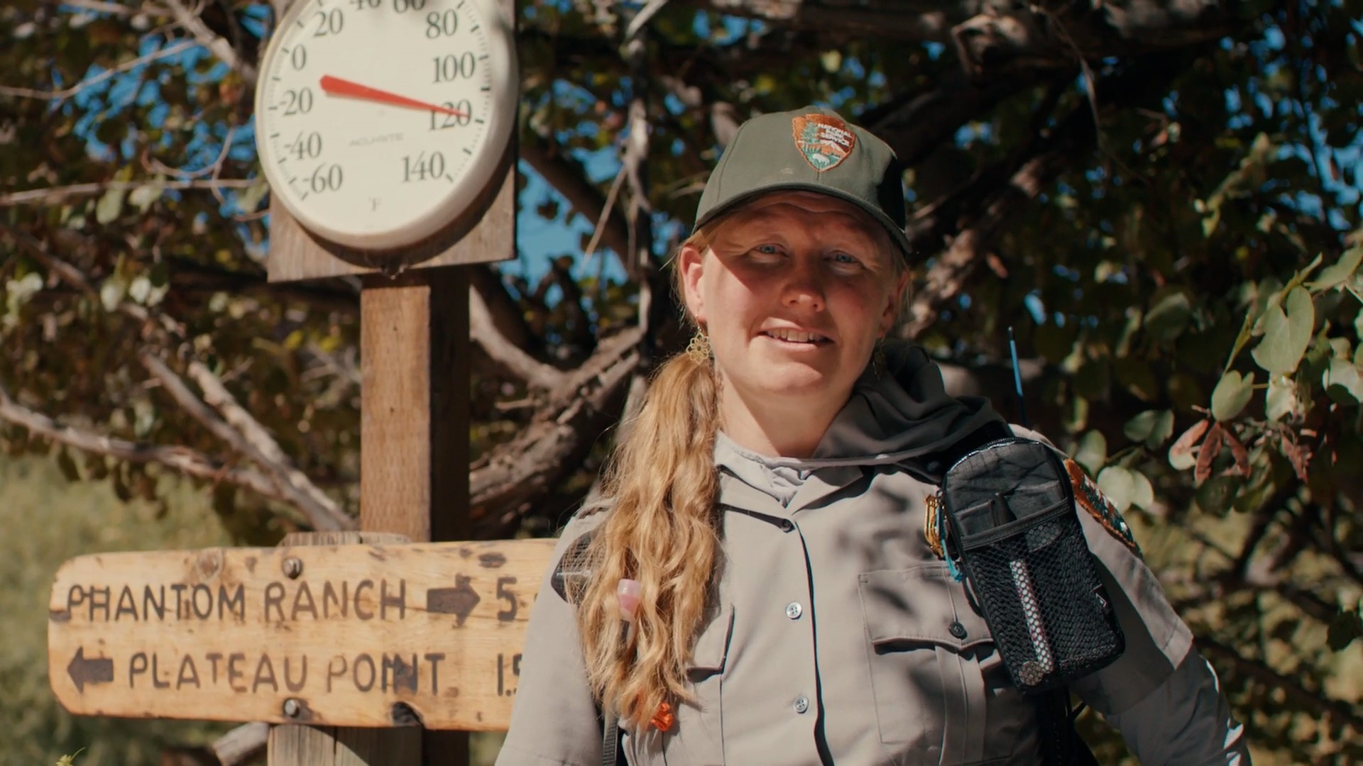 A ranger stands in front of a thermometer reaching 120+ degrees fahrenheit.