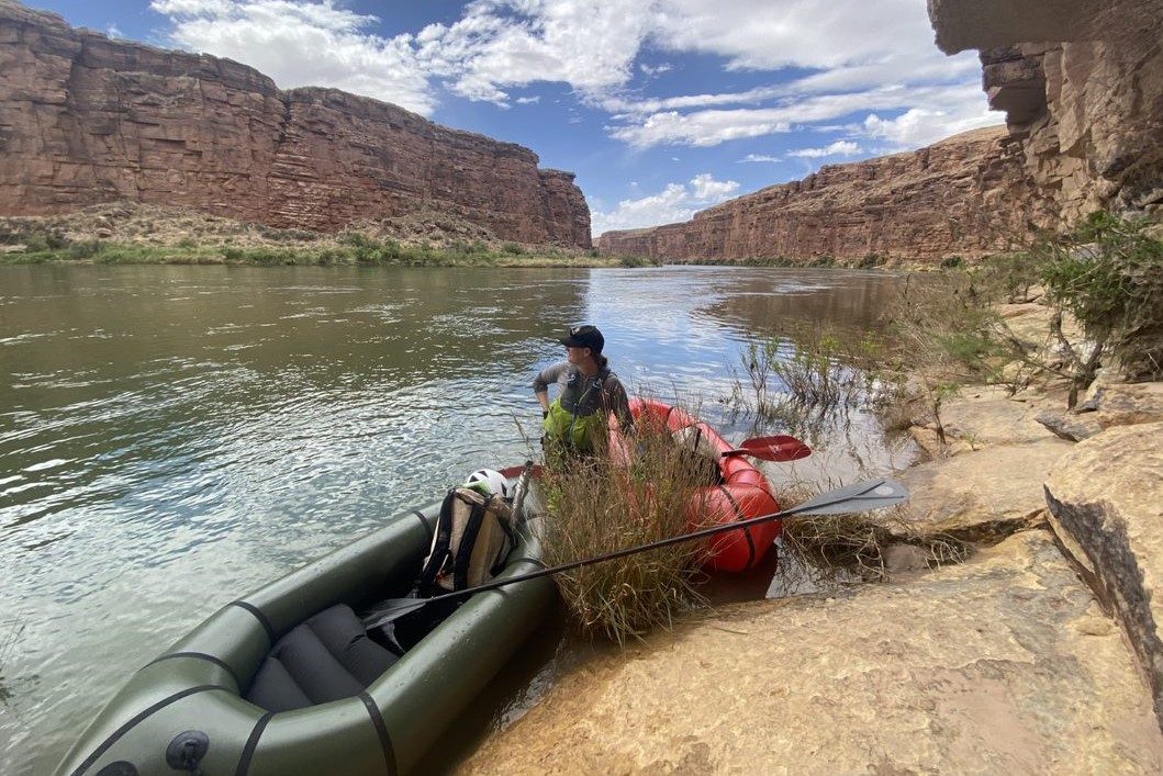 Packrafting in the Grand Canyon a woman stands on a riverbank next to two inflatable rafts