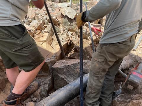 Two workers bend down over an open hole to excavate a piece of