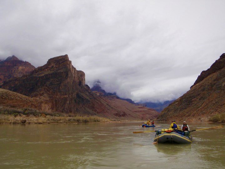 Two boats float in the Colorado River with steep canyon walls on either side