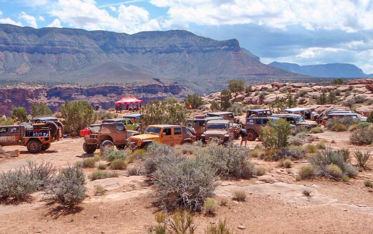 In an desert area, about two dozen vehicles are parked closely together.