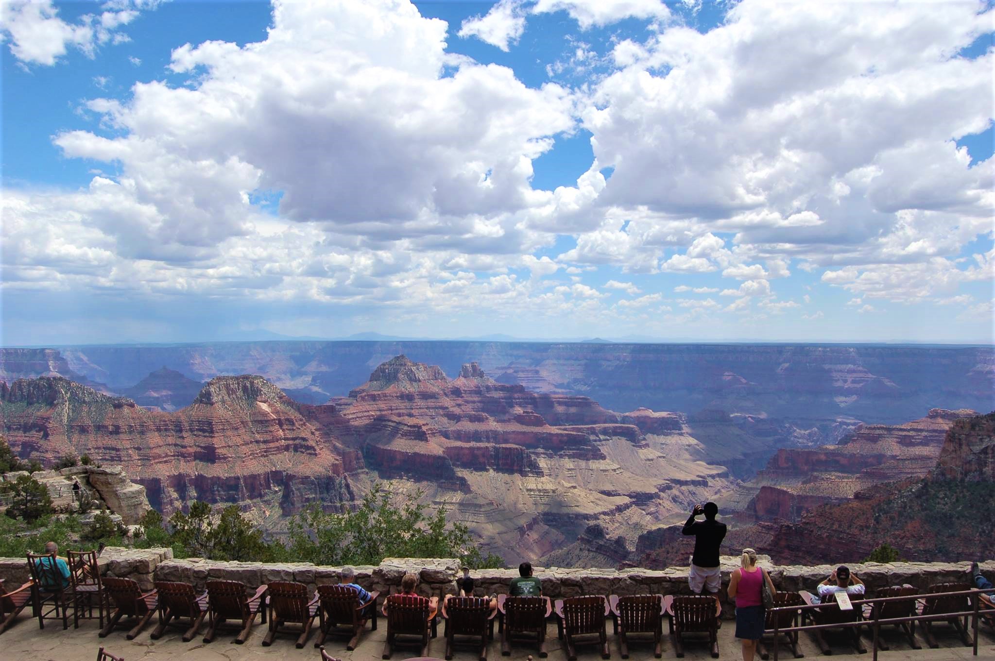 Visitors sit on chairs overlooking a canyon landscape from the North Rim Lodge
