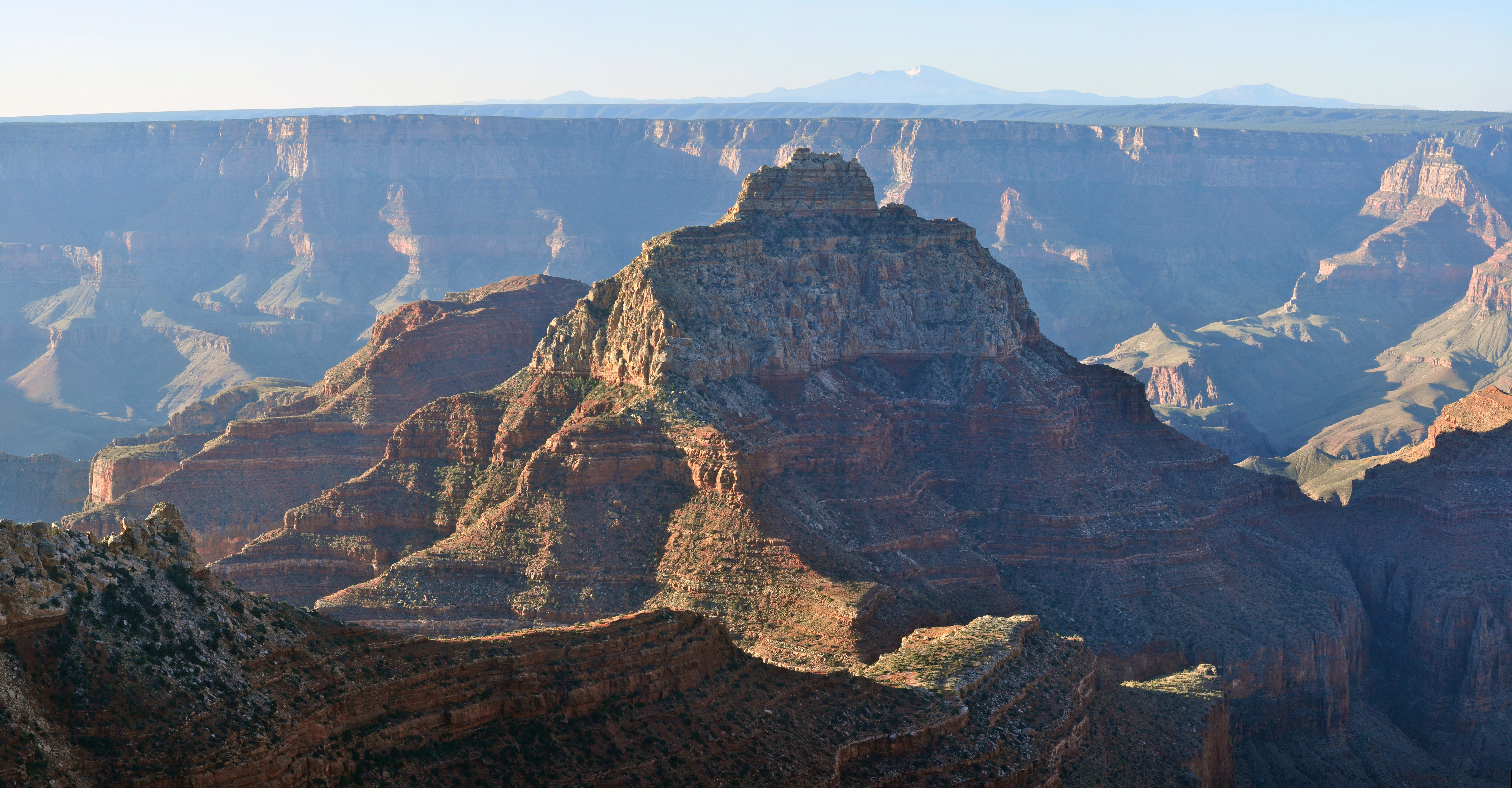 Sunrise view of the canyon from the North Rim of the canyon with mountains visible in the distance.