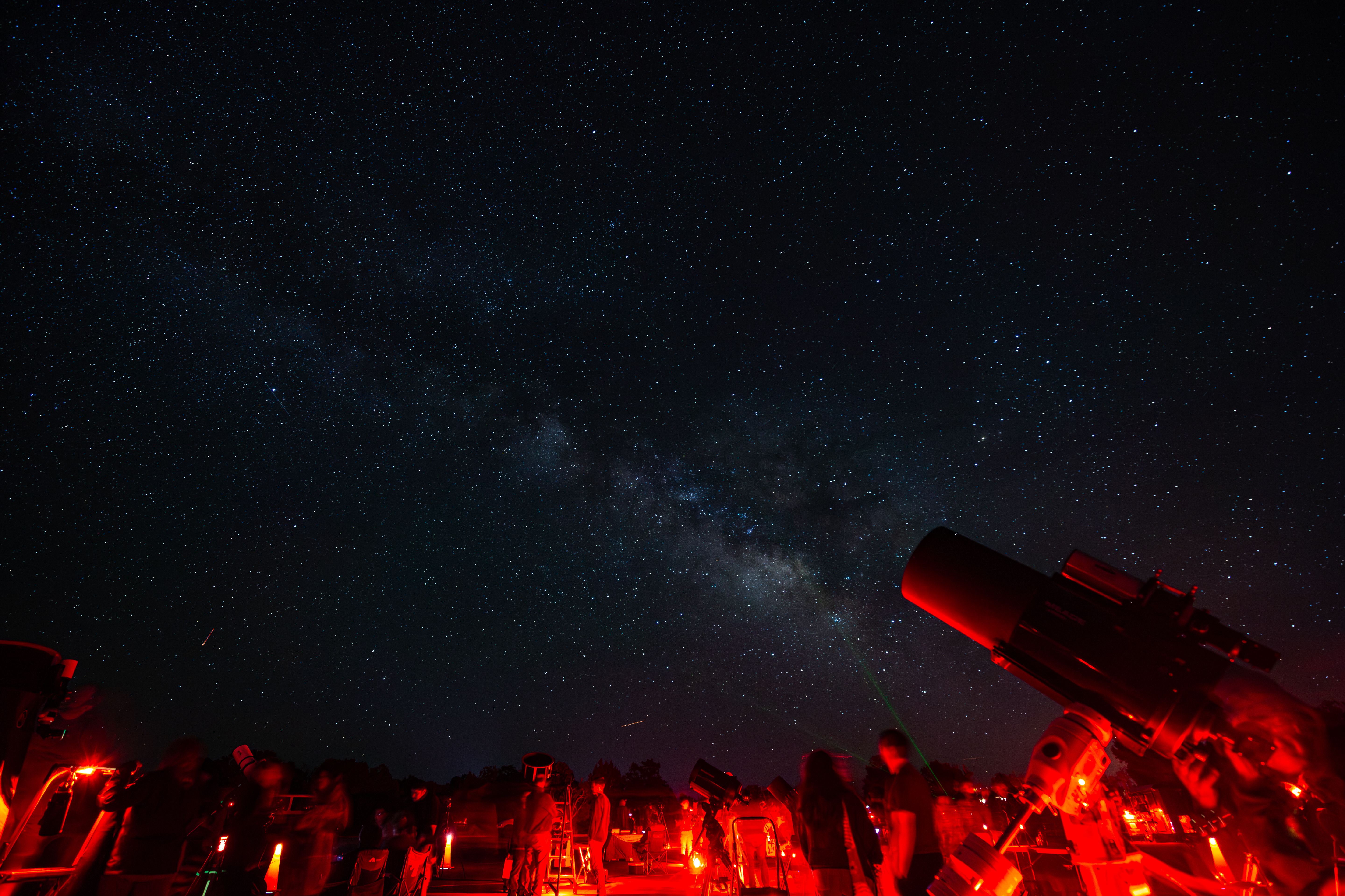 Red light illuminates a series of telescopes that are aimed at the night sky with stars and constellations