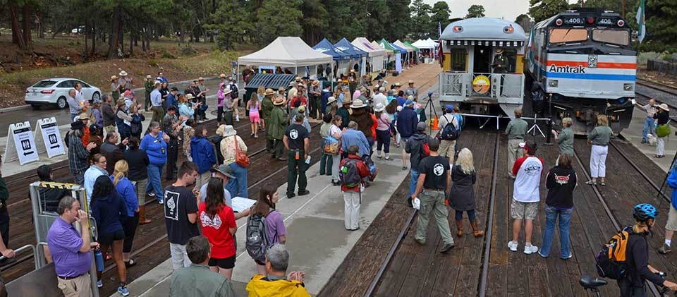Colorful crowd of people at train depot listening to speeches. Two trains are on the right and to the left of trains is a row of exhibitor tents. Colorful crowd of people at train depot listening to speeches. Two trains are on the right and to the left of trains is a row of exhibitor tents.