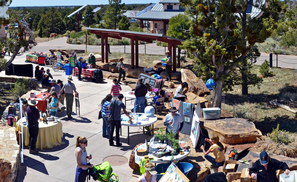 An outdoor open-air plaza with people viewing a number of Earth Day related exhibit posters and items on tables.