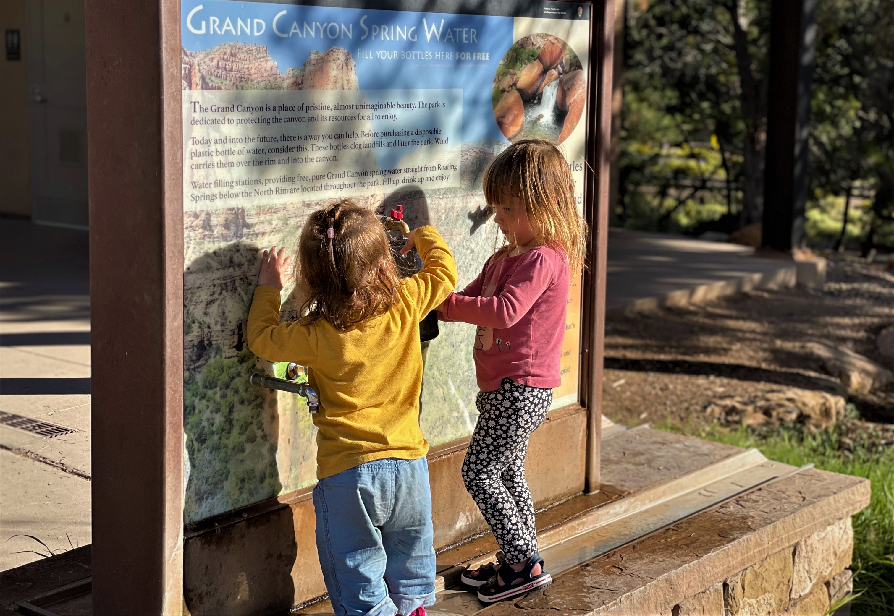 Two young junior rangers fill their water bottles at the water filling station near the Bright Angel Trailhead