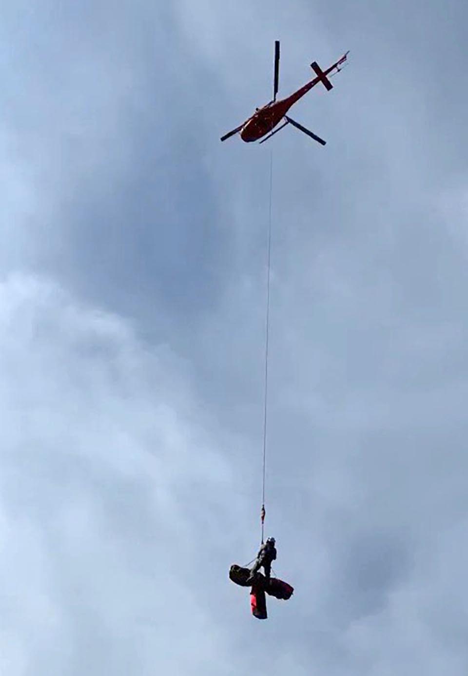 A flying helicopter carries a patient and ranger out of the canyon via a rope.