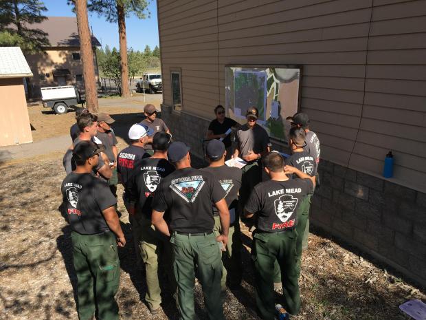 14 firefighters discuss the day's operations in front of a map