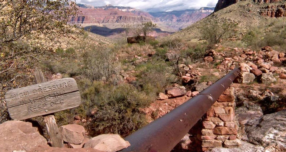 Large water pipeline runs through Grand Canyon NP over a drainage. Sign reads high pressure water line keep off