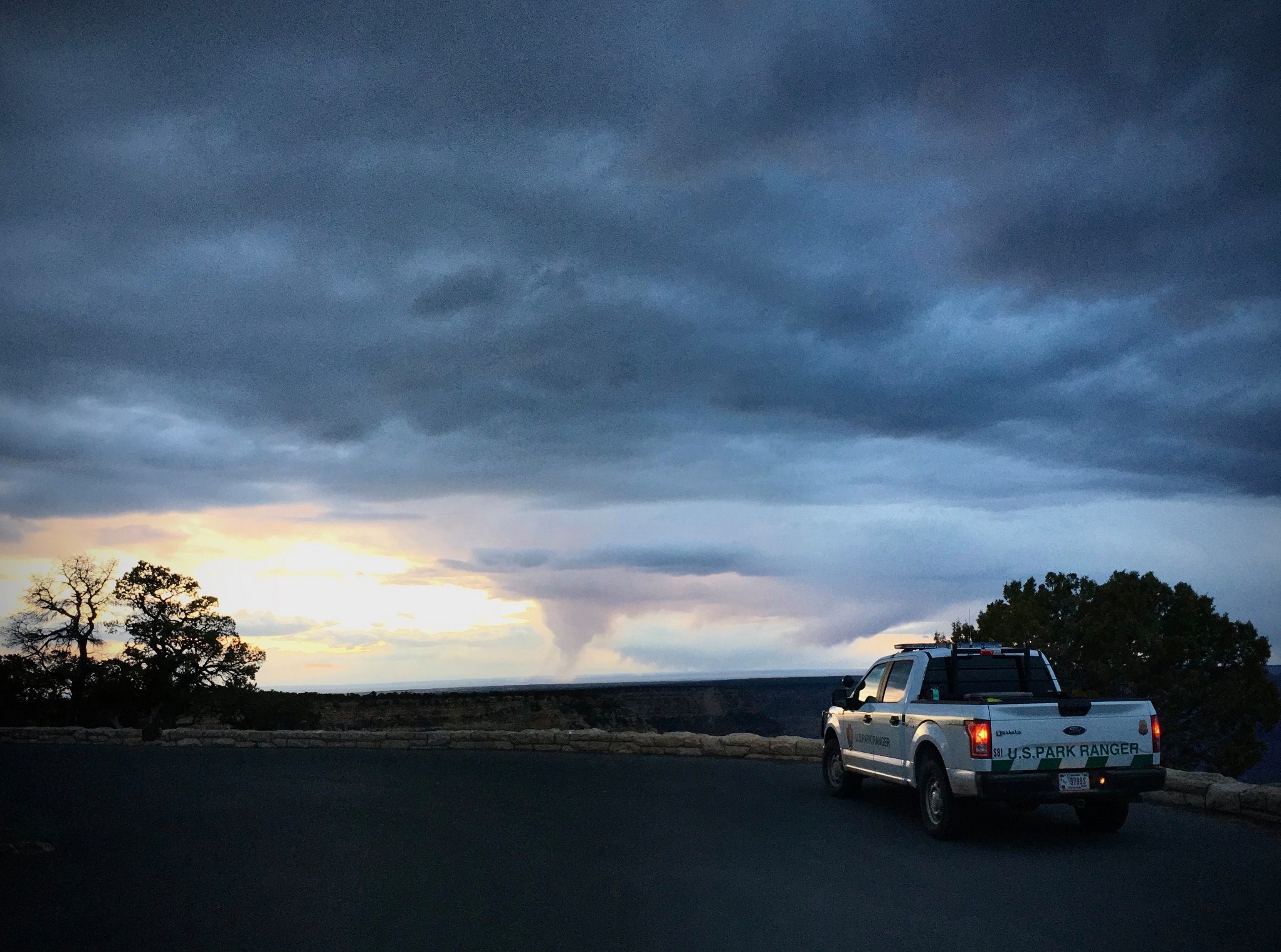 A ranger vehicle is parked on the rim of the canyon at an overlook