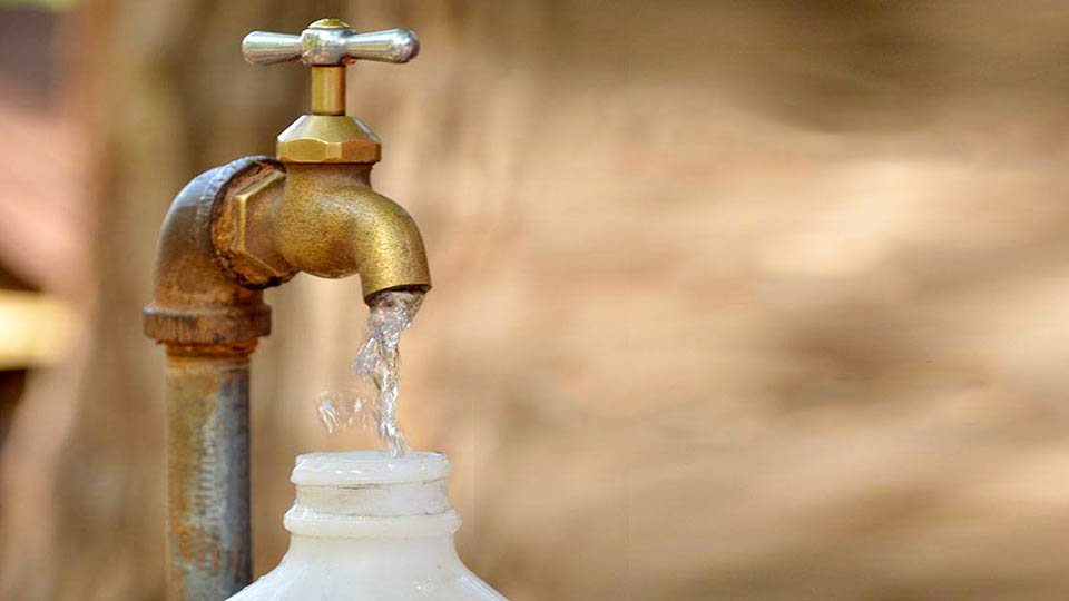 Water flowing from a brass faucet into a white water bottle