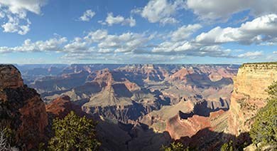 a view looking out across Grand Canyon on a sunny day with clouds in the distance.