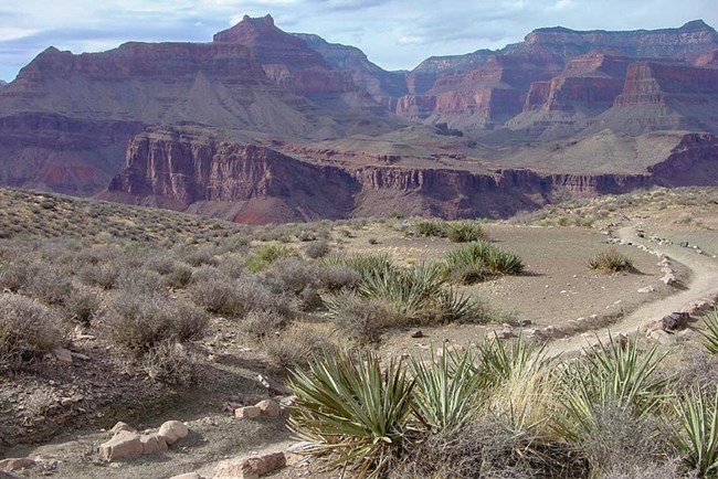 a backcountry trail crossing a desert plateau, with colorful cliff and peaks in the distance.