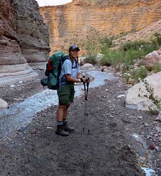 Ranger Sara poses on a backpack along a small creek.